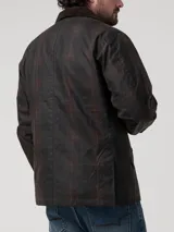 Chaqueta encerada de estilo clásico, color marrón oscuro, con cuello de cotelé y cierre frontal mediante broches a presión. Presenta un diseño de corte regular con bolsillos laterales integrados.
