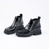 Bota corta de cuero vacuno color negro, con diseño de punta cuadrada y suela de goma tipo track. Presenta doble cierre metálico lateral y una estética robusta y moderna.