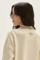 Sweater tejido de lambswool color beige, con cuello redondo y puños acampanados con rayas de colores (marrón, mostaza, bordó y beige). Incluye un detalle de temporada hecho a mano en la espalda.