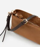 Bolso bandolera de tamaño mediano confeccionado en gamuza sintética color marrón tostado. Presenta un formato rectangular estructurado, cierre superior con cremallera y correa larga ajustable en color marrón oscuro. Incluye un detalle decorativo de tiras anudadas en uno de los laterales.