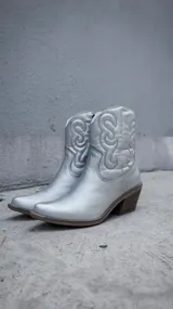 Botas texanas de caña corta en color plateado metalizado, con diseño de costuras decorativas en el lateral y taco cuadrado de madera.