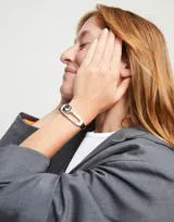 Pulsera Uno de 50 con cordones de cuero negro, pieza central bañada en plata con cristal facetado color gris y cierre de nudo corredizo con cuentas plateadas.