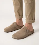 Ojota mule masculina de cuero con acabado de gamuza, diseño cerrado al frente y abierto en el talón. Cuenta con tira lateral con hebilla metálica ajustable y suela dentada de goma.