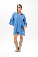 Vestido corto azul, estilo camisero, con cuello camisero, cierre frontal con botones y mangas acampanadas con volados. Presenta un diseño holgado con cortes fruncidos en el cuerpo.