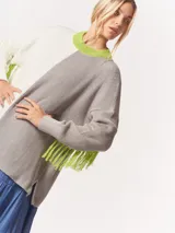 Buzo tejido oversized con bloques de color blanco y gris, cuello redondo en verde neón, tajos laterales y flecos verdes en las mangas.