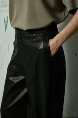 Pantalón de cuero sintético negro de corte ancho y tiro alto, con costuras verticales decorativas en el frente y cierre frontal con botón.