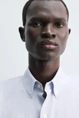 Camisa de corte regular fit confeccionada en popelín de algodón. Presenta cuello abotonado, manga larga con puños ajustables mediante botón y cierre frontal de botonadura completa.