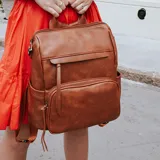 Mochila de símil cuero color marrón, con apertura superior, dos bolsillos frontales con cierre metálico y bolsillos laterales. Incluye tres bolsillos internos y correa extraíble.