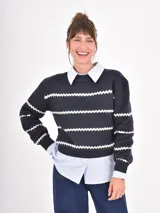Buzo de tejido de punto en color azul marino con rayas horizontales blancas en diseño de zigzag. Presenta cuello redondo, mangas largas y puños acanalados.