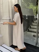 Vestido largo de tejido de punto con diseño de rayas verticales en blanco y negro. Presenta escote en V, mangas cortas y tajos laterales en el ruedo para mayor movimiento.