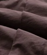 Campera tipo parka color marrón con capucha estructurada, cierre frontal y bolsillo vertical con cierre en el pecho. Presenta detalles de estampado utilitario en el frente y recortes en el cuerpo.