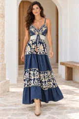 Vestido largo de denim azul con diseño de paneles alternados entre tela lisa y estampados florales en tonos beige. Cuenta con tirantes finos, escote en V y una faja tejida en la cintura con cordón ajustable y borlas.