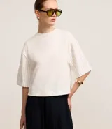 Remera boxy de mangas cortas amplias, color blanco, confeccionada en algodón, con cuello redondo y rayas verticales en las mangas y en la espalda.