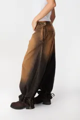 Jean de corte wide leg con efecto degradado en tonos marrón y negro. Presenta costuras verticales frontales y un diseño de puño ajustable en el bajo de la pierna.