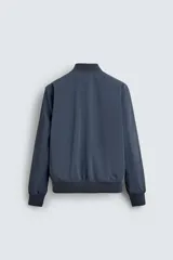 Cazadora bomber ligera de tejido técnico color verde oliva, con cuello, puños y bajo en rib elástico. Presenta cierre frontal de cremallera y bolsillos de vivo en la cadera.