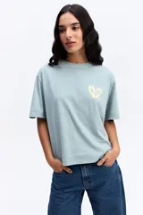 Remera de corte oversize color verde agua con efecto acid wash, cuello redondo y estampa pequeña en el pecho. Presenta una silueta relajada y mangas cortas.