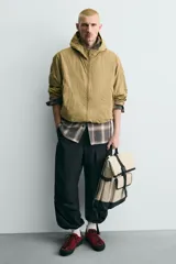 Mochila verde militar con acabado engomado, solapa superior con cierre de hebilla y cremallera, bolsillo frontal con cierre imantado, compartimento interno para laptop de hasta 13 pulgadas, asa de mano superior, correas de hombro ajustables y espalda acolchada. Base de cuero sintético negro.