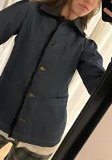 Blazer de jean azul con cuello, solapa y cuatro botones frontales. Presenta volados de encaje negro en cuello y delantero, mangas largas con pliegues y bolsillos plaqué. Interior con terminación en hilo bordó.