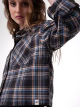 Camisa de franela a cuadros en tonos negro, celeste y amarillo, de corte cropped y amplio, manga larga, cuello camisero, bolsillos frontales en el pecho y cierre de botones.