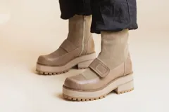 Botas de caña media en combinación de cuero liso y gamuza color visón. Presentan una suela track con plataforma y taco cuadrado, cierre lateral y una tira con velcro sobre el empeine.
