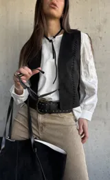 Chaleco negro de gamuza sintética, de estilo boho-chic, con costuras decorativas en los bordes y diseño clásico atemporal.