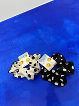 Colita de pelo tipo scrunchie de tela negra con estampado de lunares blancos.