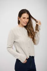 Saco de punto gris claro con textura acanalada, cuello redondo, cierre frontal con botones y bordes con terminación ondulada.