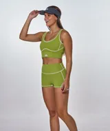 Conjunto deportivo compuesto por un top y un short de tiro alto en color verde oliva. El top presenta escote redondo y costuras decorativas en contraste, mientras que el short cuenta con un diseño ajustado con costuras visibles y logo estampado en el top.