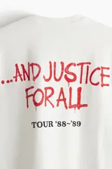 Remera de algodón color blanco crudo, corte oversized y manga corta. Presenta un estampado frontal grande con el logo de Metallica y la ilustración de Lady Justice, con el texto "AND JUSTICE FOR ALL" y "TOUR '83-'89".