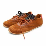 Championes de gamuza color marrón con detalles en cuero liso del mismo tono. Presentan cordones bicolores en naranja y negro, suela de goma plana y un detalle en color rojo en la parte trasera del talón.