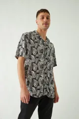 Camisa de manga corta con cuello cubano, confeccionada en viscosa con estampado de hojas en tonos azules. Presenta cierre frontal abotonado y corte slim.