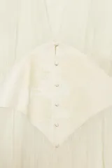 Blusa semitransparente de cuello solapa con escote en pico y manga larga tipo murciélago. Presenta un panel central con botones forrados y detalle de aplicación de encaje a tono. El bajo tiene un acabado asimétrico.