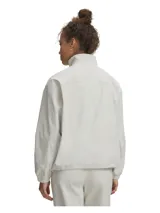 Campera Under Armour Unstoppable Wvn Fz de color gris claro, confeccionada en tejido técnico con tecnología UA Storm que repele el agua. Presenta cuello alto, cierre frontal completo, hombros caídos, bolsillos laterales con cierre y puños y bajo elásticos con cordón ajustable.
