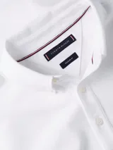 Chomba blanca de piqué con textura tipo diamante, cuello tipo chomba, cartera de cinco botones y logo de Tommy Hilfiger bordado en el pecho.