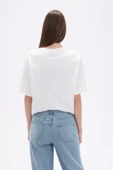 Remera de algodón color blanco, de corte holgado y manga corta, con cuello a la base. Presenta un estampado frontal rectangular en tonos amarillos y verdes con motivos botánicos, realzado con detalles bordados y lentejuelas.