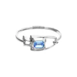 Pulsera semirrígida de aleación de metales bañada en plata, con diseño de eslabón central y cristal facetado de corte rectangular en color azul.