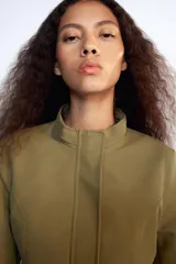 Cazadora entallada Zara color verde militar, con cuello alto, manga larga y bajo acabado en peplum. Cuenta con cierre frontal oculto con cremallera y botones a presión.