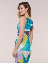 Vestido midi de silueta al cuerpo confeccionado en tul elastizado, con escote redondo, diseño sin mangas, frunces laterales en la cintura y forro interior a tono. Presenta un estampado geométrico multicolor en tonos verde, turquesa, violeta y blanco.
