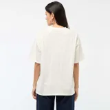 Camiseta de cuello redondo y manga corta, color blanco hueso, con estampado central metalizado en tono oro rosa del personaje Stitch sosteniendo un corazón.