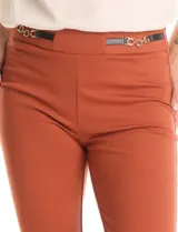Pantalón de tiro alto con silueta de pierna recta, confeccionado en tejido elastizado. Presenta una pretina con apliques laterales de ecocuero y cadena dorada decorativa.