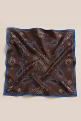 Pañuelo cuadrado de seda con estampado de estilo western que combina motivos florales de rosas y patrones paisley en tonos marrones, con detalles en azul y blanco. Presenta bordes en color azul y terminaciones hechas a mano.