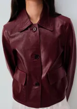 Chaqueta de cuero de corte recto con cuello camisero, cierre frontal de botones y dos bolsillos de parche con solapa en la parte delantera.