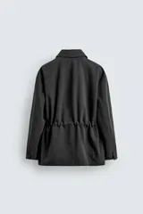 Cazadora relaxed fit de hombre, confeccionada en tejido técnico con algodón de color negro. Cuenta con cuello camisero, manga larga y bolsillos frontales de plastrón con solapa. Presenta cintura ajustable con cordón interior y cierre frontal con cremallera oculta por solapa con botones a presión.