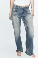 Jeans de tiro bajo y cinco bolsillos, con diseño de pierna ancha y larga. Presenta roturas y desgastes sutiles en la parte delantera. Cierre frontal con cremallera y botón metálico.
