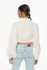 Top corto de lino italiano con diseño a cuadros en tonos verde oliva, beige y rosado, cuello camisero, mangas largas abullonadas con puños elásticos y nudo frontal ajustable.