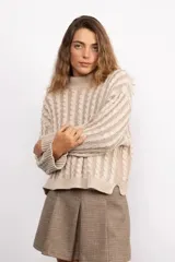 Sweater de punto con diseño de trenzas verticales, cuello redondo y silueta oversize. Presenta mangas largas con puños acanalados y un corte recto a la altura de la cadera.