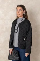 Campera corta de diseño capitoneado con patrón de rombos, color negro. Presenta cuello redondo, cierre frontal abierto, mangas largas y dos bolsillos delanteros con detalle de broche.
