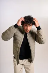 Campera puffer de corte clásico en color beige, con cierre frontal, cuello alto y puños elásticos. Presenta un diseño acolchado horizontal y un pequeño logo bordado en el pecho.