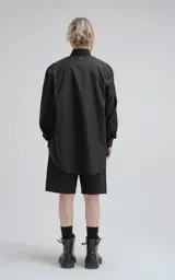 Camisa negra de manga larga, confeccionada en poplín de algodón. Presenta un calce oversize, cuello camisero, cierre frontal de botones y dos bolsillos cuadrados superpuestos en el lado derecho del pecho.