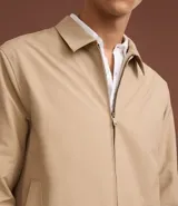 Campera de sarga color beige con cuello inglés, cierre frontal de cremallera, mangas largas y bolsillos laterales. Diseño minimalista y versátil con forro interior.